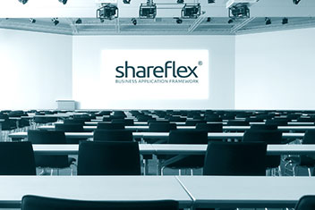 Veranstaltungsraum mit Stuhlreihen und Tischen sowie dem Shareflex-Logo auf einer Leinwand.