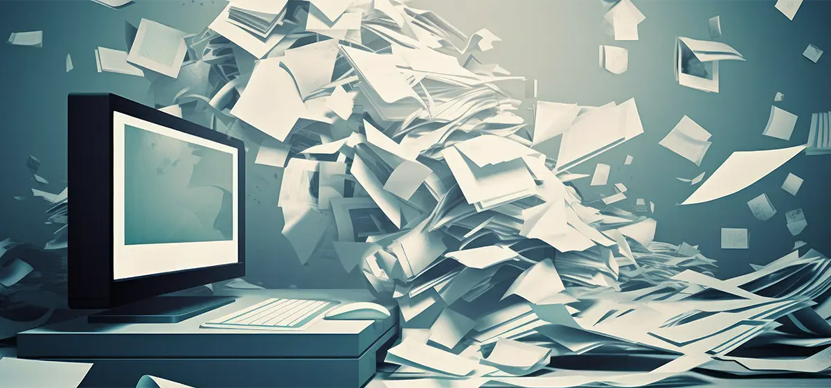 A large pile of paper and documents blown towards a computer.