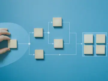 Eine Hand die einen Holzquader am Anfangspunkt eines Prozessdiagramms aus weiteren Holzquadern platziert.